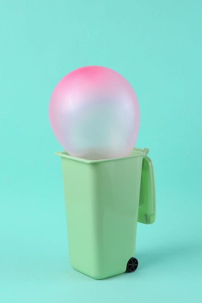 Pink balloon in trash can on bright blue background