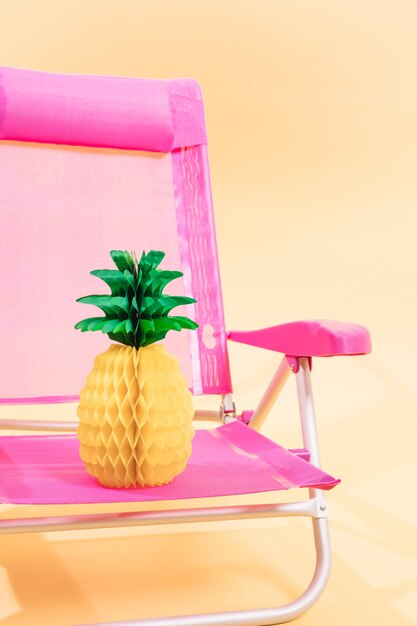 Pink beach chair with a paper pineapple on it on light orange background