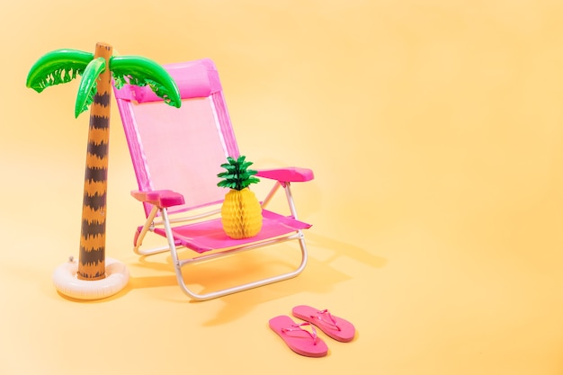 Pink beach chair with a paper pineapple on top of it pink flipflops and an inflatable palm tree