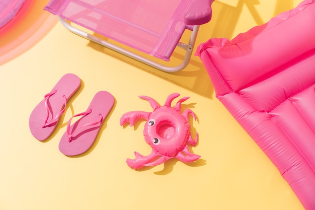 A pink beach chair with pink flip flops a pink inflatable mat and a pink inflatable crab  Top view