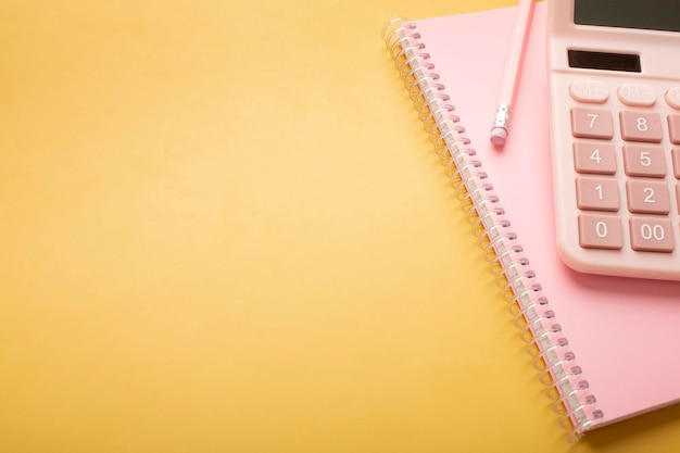 Pink beautiful notepad calculator and pencil on a yellow background with a place for an inscription