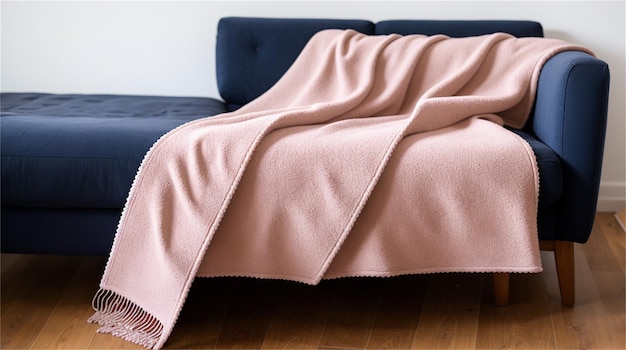 A pink blanket on a blue couch with a white wall behind it.