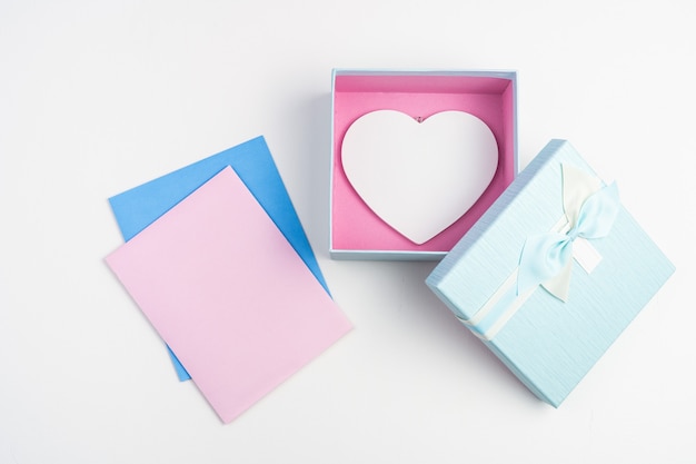 Pink and blue envelopes and gift box with white heart on light background.