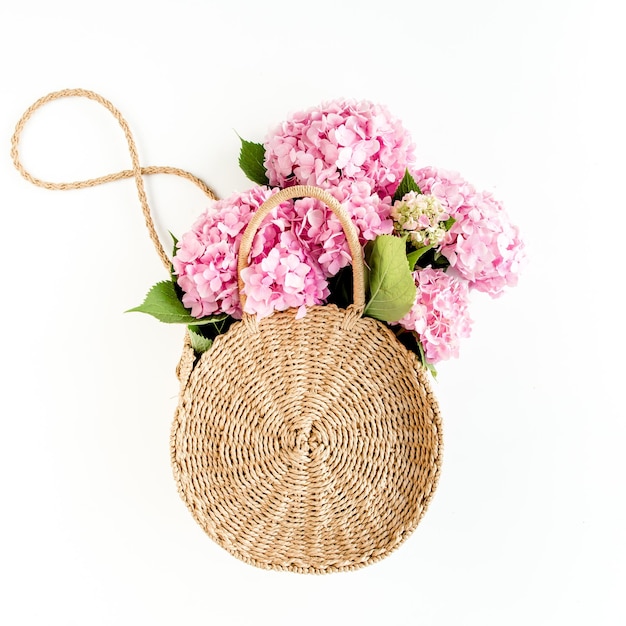 Pink bouquet of hydrangea in a straw bag on white background minimal floral concept flat lay top vie