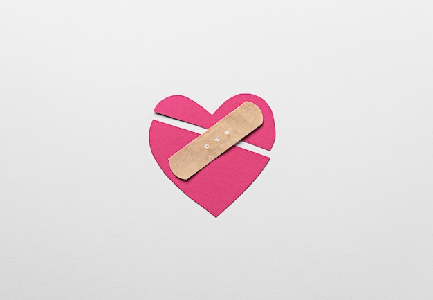 Pink broken heart with band aid flat lay