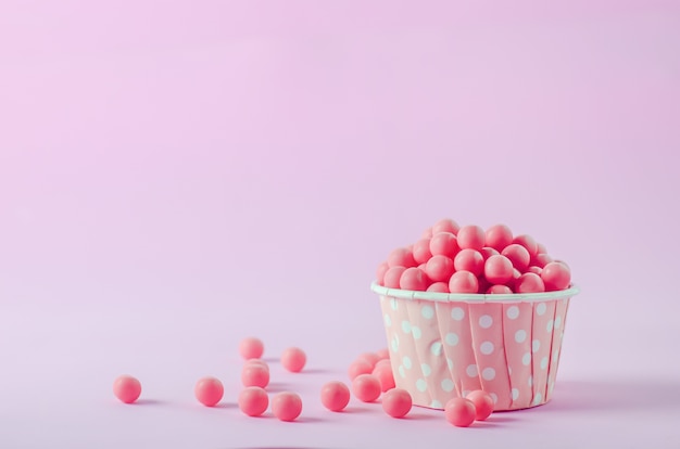 Pink candies in pink paper cup with white polka dot pattern on pink background