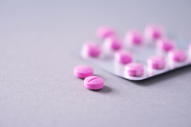 Pink capsule, pills, vitamins on grey background. Copy space. Bunch of drugs, cold flu treatment. Women disease treatment.