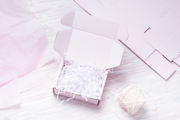 Pink Cardboard Carton box with paper filler on white wood background