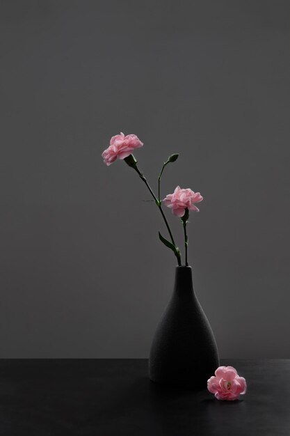 Photo pink carnations in black vase on black table