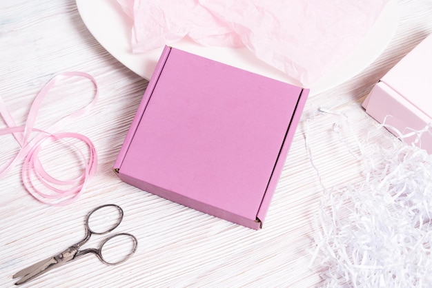 Pink carton, cardboard box with filler on wooden desk