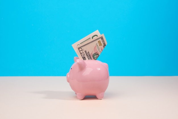 Pink ceramic piggy bank with paper us dollars on a blue backgrou