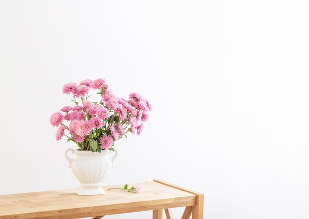 Pink chrysanthemums in white vase on white interior