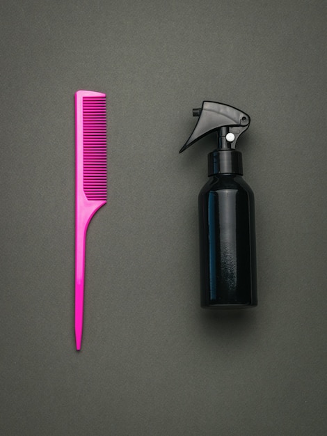 Photo pink comb and spray with hair product on a dark background. a tool for hair care. flat lay.