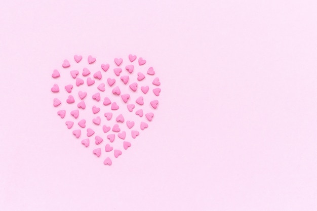 Pink confectionery sprinkles in heart shape on pastel pink background