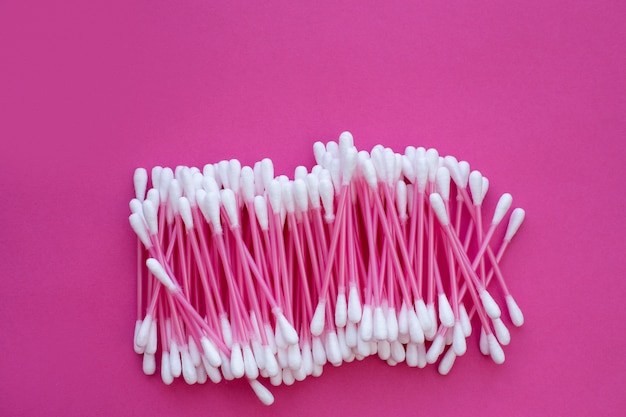 Pink cotton buds with white heads laid out on a pink background