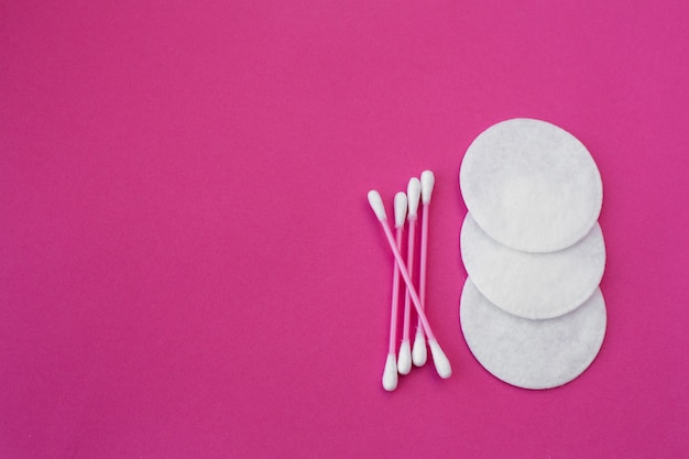 pink cotton buds with white heads and white round cotton disks laid out on a pink background