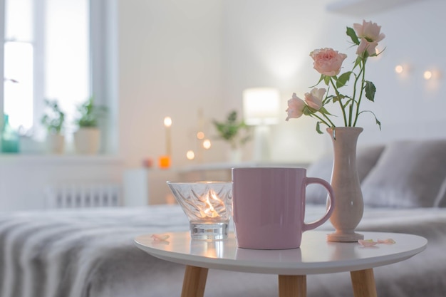 Pink cup of coffee and  roses  in vase on table in bedroom