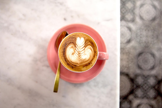 Pink cup of hot cappuccino on white marble table