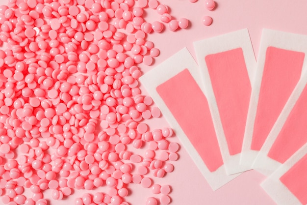 Pink depilation hot wax granules and wax depilatory strips for delicate areas on a pink background