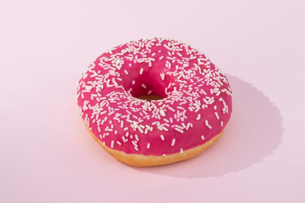 Pink donut with icing on pastel pink background.