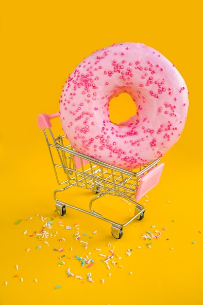 A pink donut with pink sprinkles sits in a shopping cart.