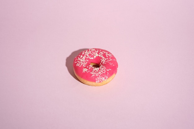 Pink donut with sprinkles, sweet glazed dessert food on pink minimal background, angle view copy space