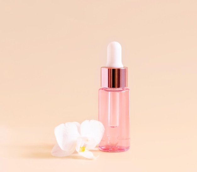 Pink Dropper Bottle near white orchid flower on light yellow close up Skincare beauty product