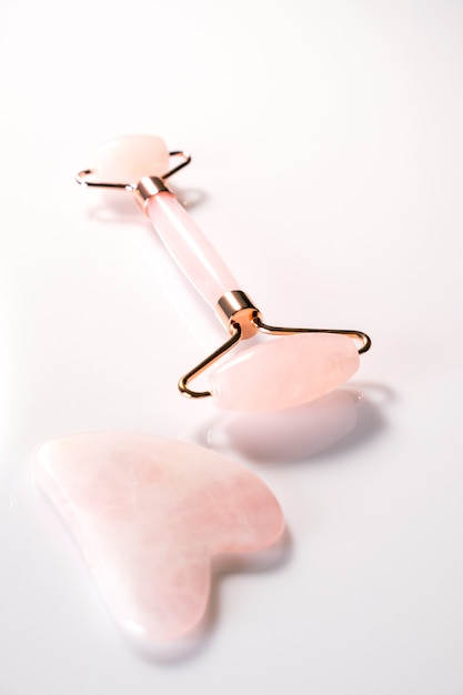 Pink face roller and gua sha massager made from natural quartz  stone over white background.  Lifting and toning treatment at home.