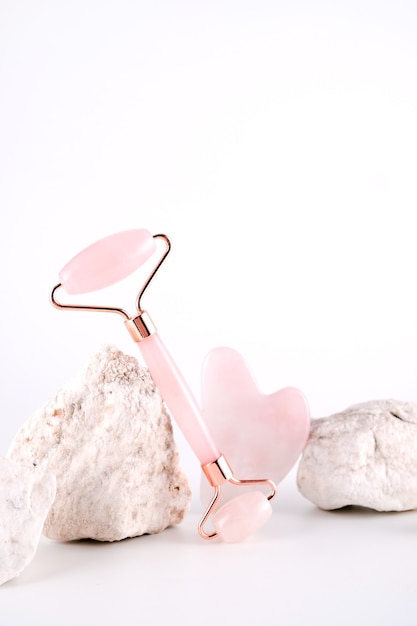 Pink face roller and gua sha massager made from natural quartz  stone over white background.  Lifting and toning treatment at home.