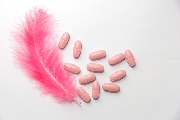 Pink feather next to pills on a white background