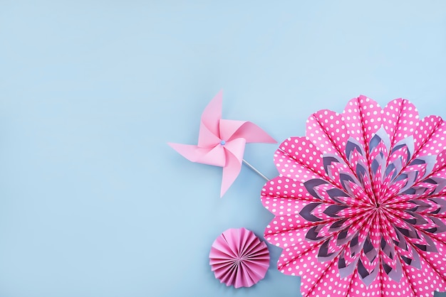 Pink flower made of paper and paper windmill on light blue wall