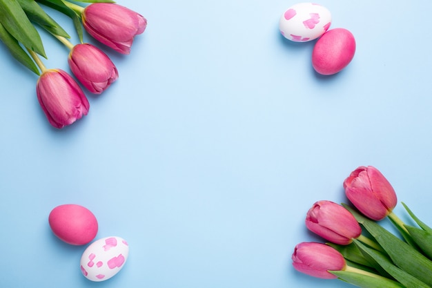 Pink flowers tulips and easter eggs on a blue surface