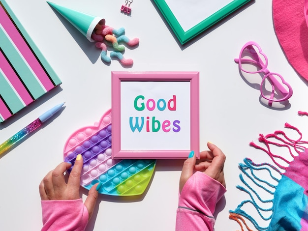 Pink frame with text Good Vibes and popit toy in hands Collection of party objects and sweets