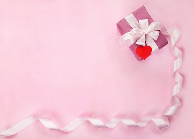 Pink gift box, white bow, long curved ribbon, paper red heart. Top view, flat lay. Valentines Day