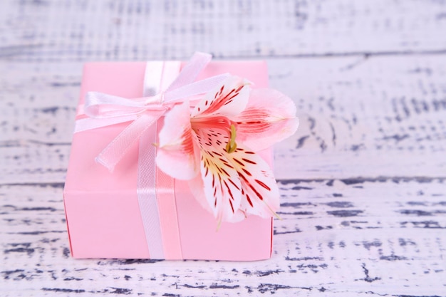 Pink gift with bow and flower on wooden table close-up