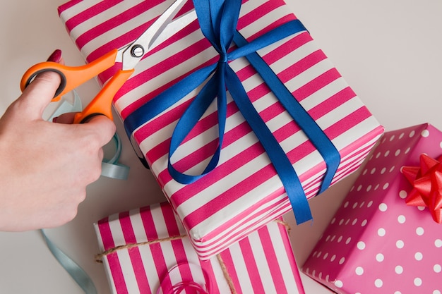 Pink gift wrapping. Birthday background. Hands packing festive boxes with blue ribbon.