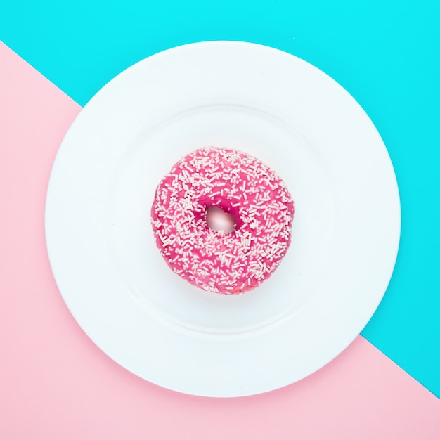 Pink glazed donut on color surface. Flat lay.