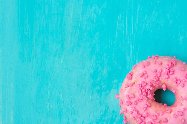 Pink glazed doughnut with sugar sprinkles in bottom corner on light blue background.