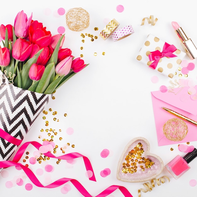 Pink and Gold Styled Desk with Florals. Pink tulips in black and white stylish wrapping paper, gifts, cosmetics and female accessories with confetti on white background