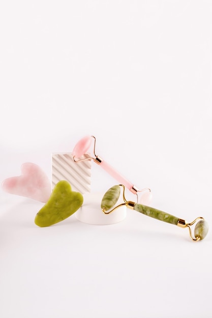 Pink and green face roller and gua sha massager made from natural  stone over white background.  Lifting and toning treatment at home.