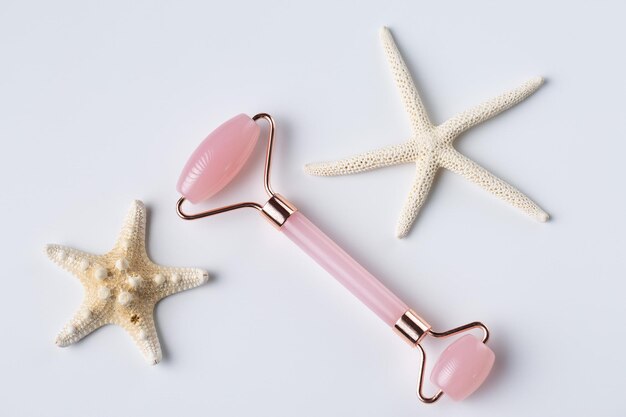 Pink Gua Sha massage tool on a white background closeup Rose Quartz jade roller Facial composition with starfish