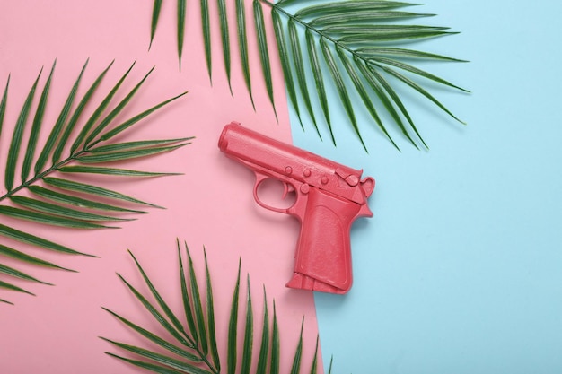 Pink gun and palm leaves on pink blue background Tropical minimal layout Top view Flat lay