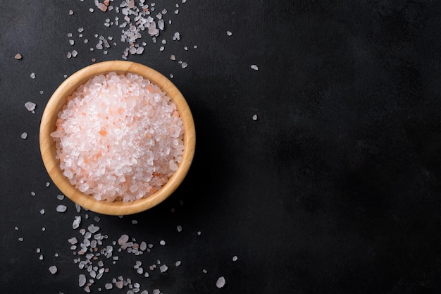 Photo pink himalayan salt in a wooden bowl with scattered salt on a black background copy space