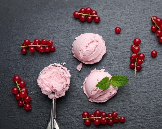 Pink ice cream balls on a black stone board red currant berries nearby top view