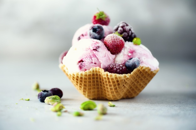 Pink ice cream with berries, strawberries, blueberries, raspberries, pistachios in waffle basket. Summer food concept, copy space. Healthy gluten free fruit ice-cream.