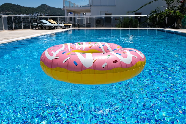 Pink inflatable donut doughnut floating mattress in swimming pool. Beach pool accessories. Summer holiday concept.