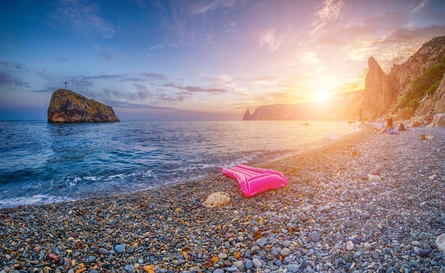 Pink inflatable mattress on the pebbles beach at sunset rocky seaside view with single inflatable