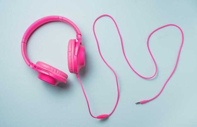 Pink large headphones with a wire on a blue background. Top view image