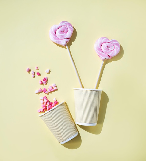 Pink lollipops in the shape of hearts at paper cup with color sugar on a yellow background Top view and copy space