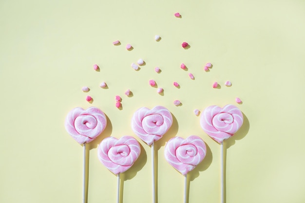 Pink lollipops in the shape of hearts with color sugar on a yellow background Top view and copy space